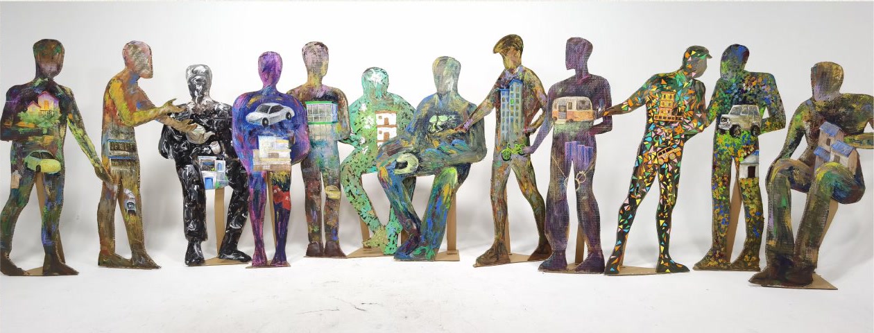 Twelve life-size painted cardboard figures standing and sitting in a row against a white wall